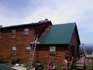 Green metal roof going on a two story log home with ladders set in Westville