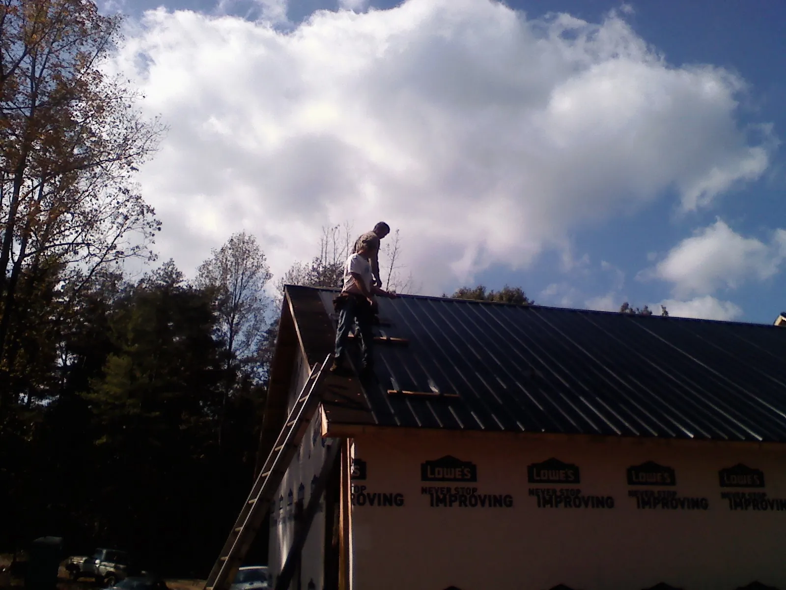 Roofer fastening dark metal panels high against a cloudy sky, from a Roof Inspection job in Westville